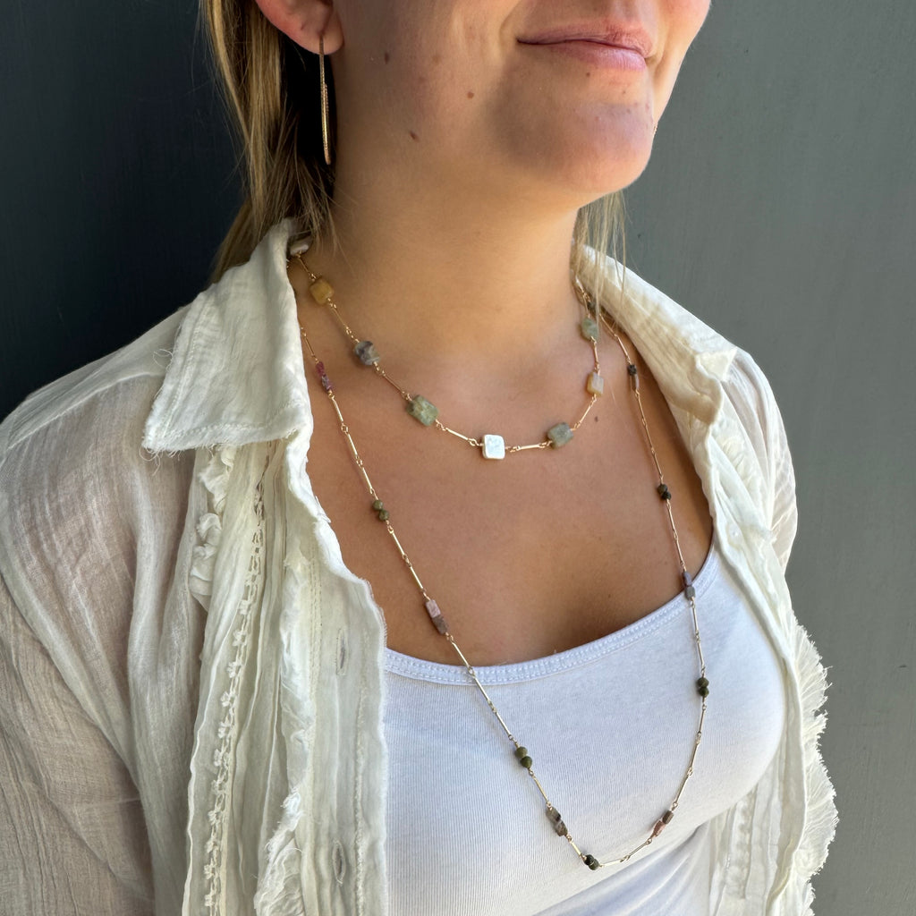 Woman wearing a layered necklace with a plain background