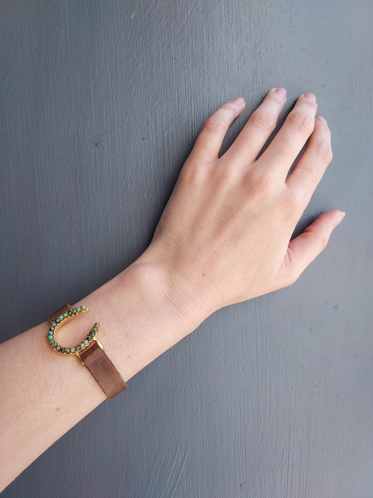 African Turquoise Horseshoe Leather Bracelet in Gold on hand model over blue background