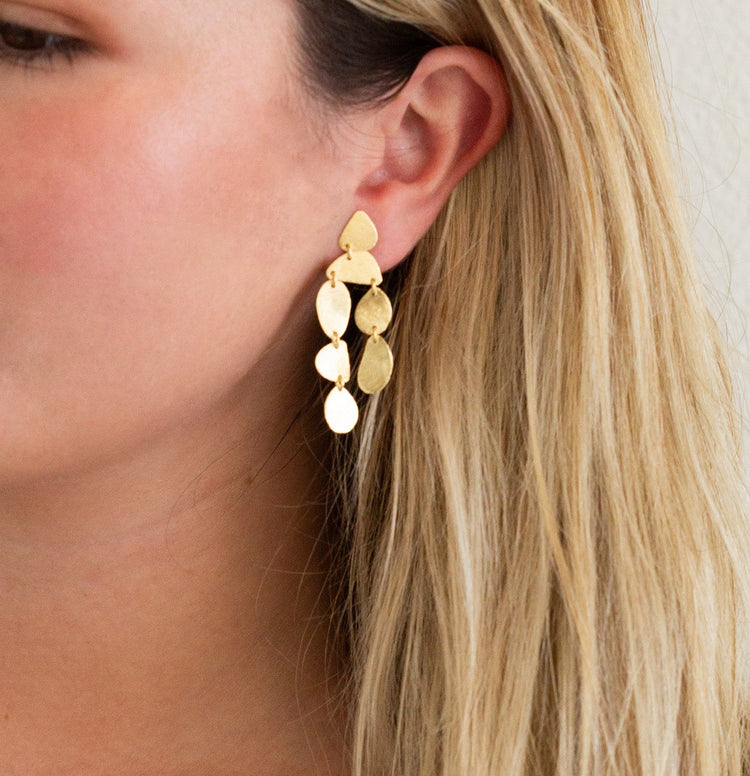 Gold leaf-shaped earrings worn by a person with blonde hair.