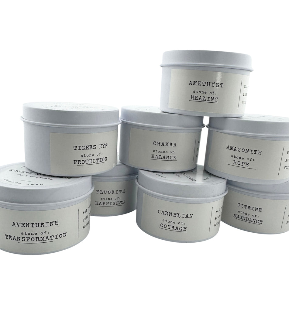 Intention candles in white tins with stones and meanings printed on labels on white background.  