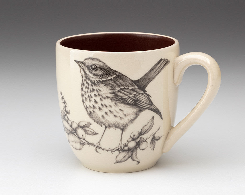 A beige ceramic mug with a floral pattern and an illustration of a hermit thrush bird perched on a branch.
