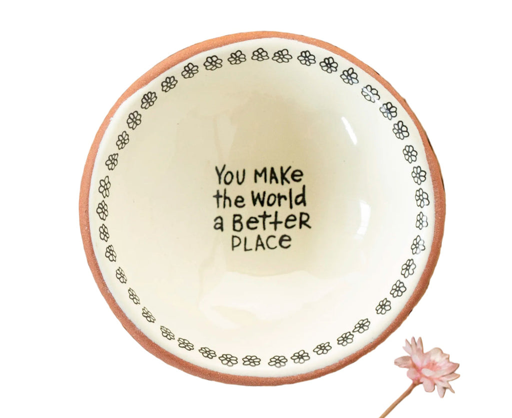 Ceramic plate with 'You make the world a better place' text on a wooden surface with flowers.
