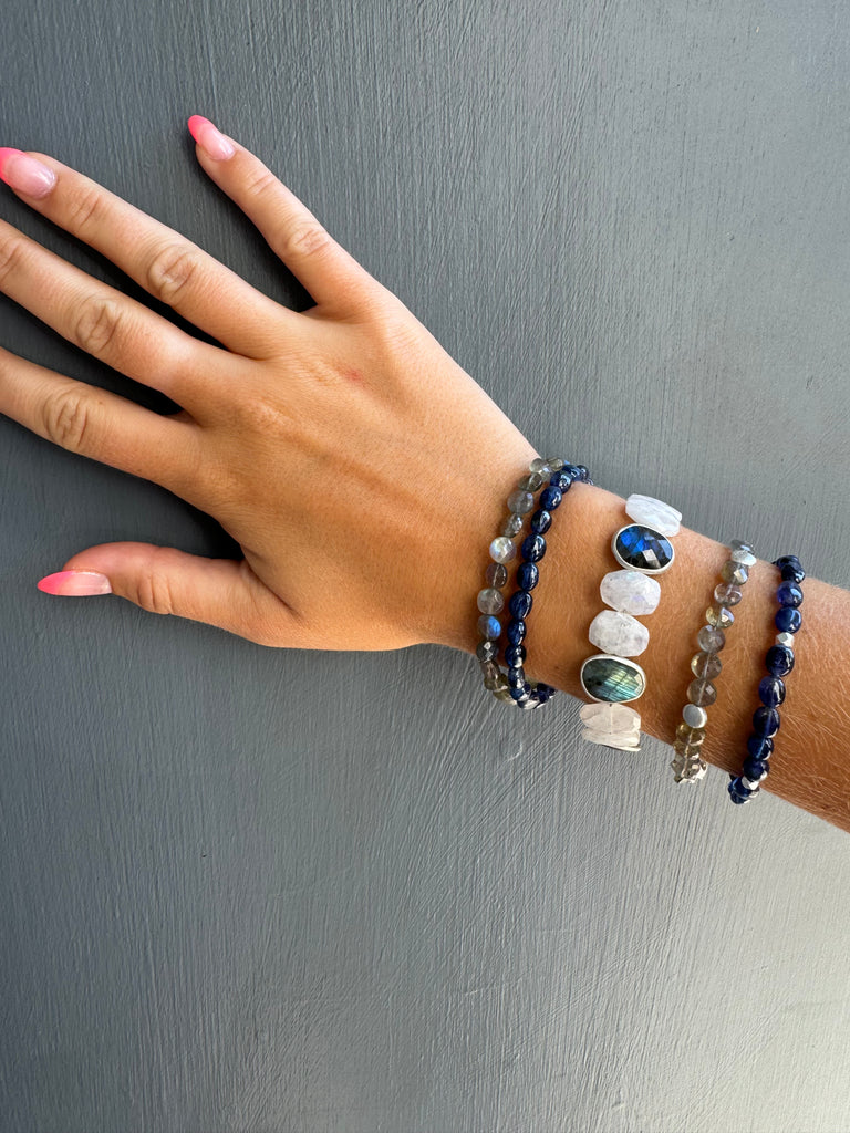 Hand wearing multiple beaded bracelets on a gray background