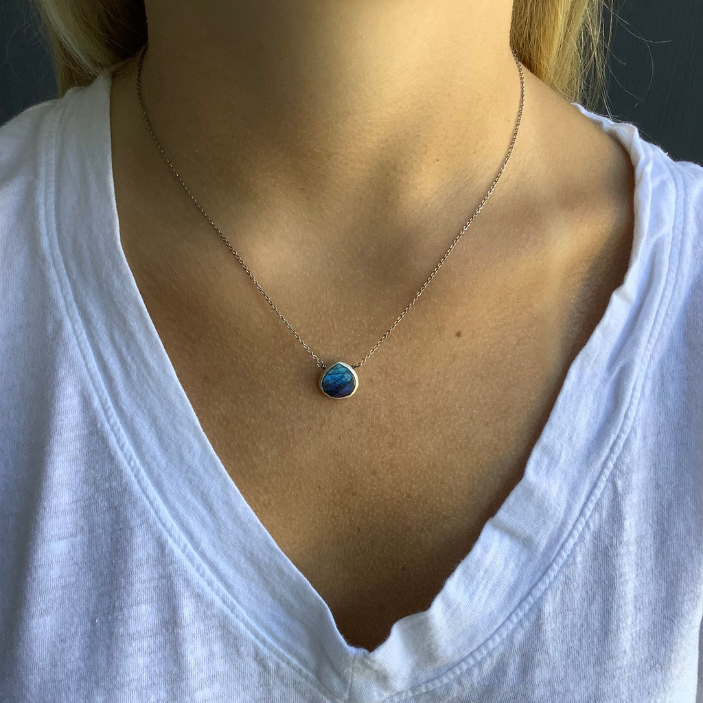 Close-up of a necklace with a blue pendant on a person wearing a white shirt.