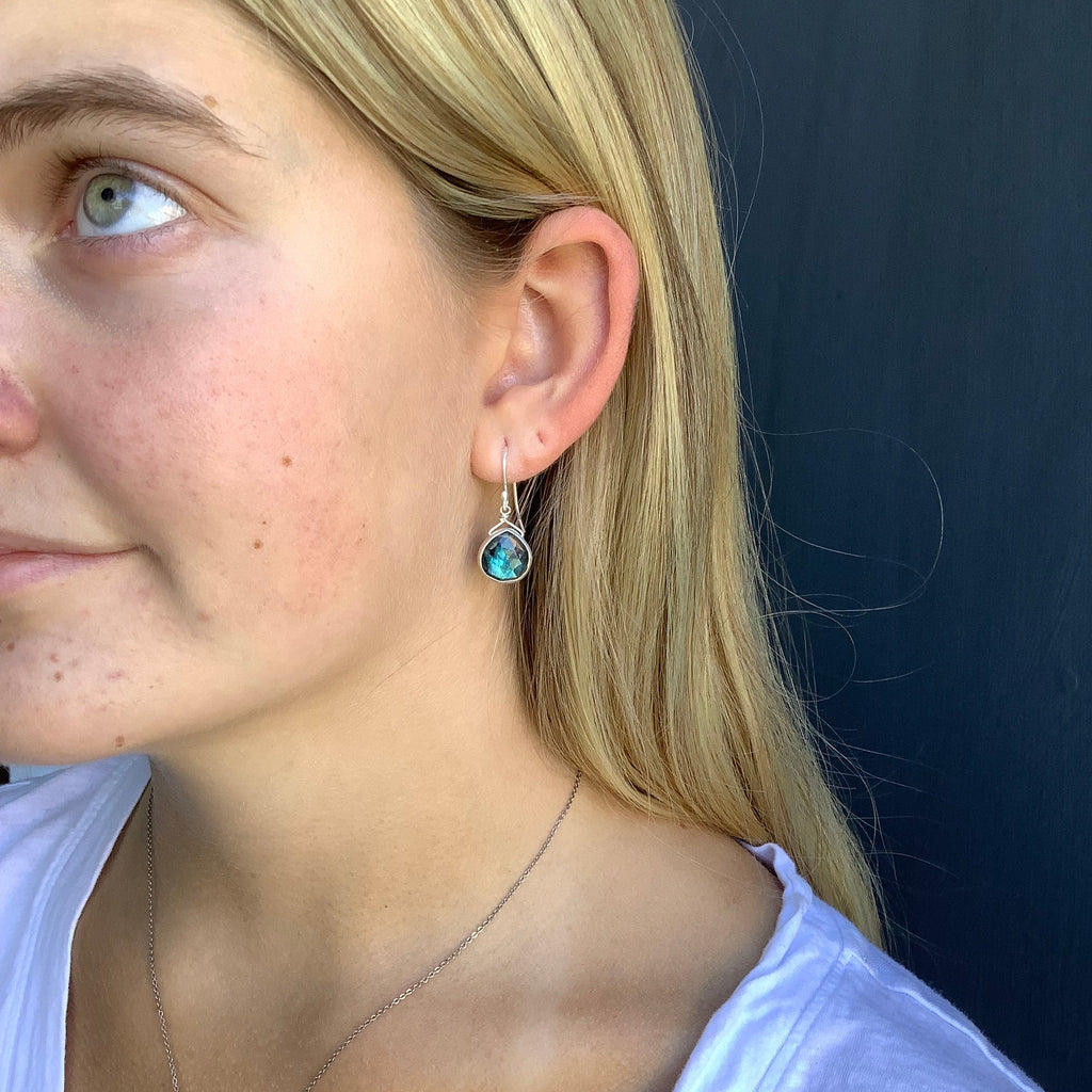 Close-up of a person wearing a silver earring with a blue gemstone against a dark background.