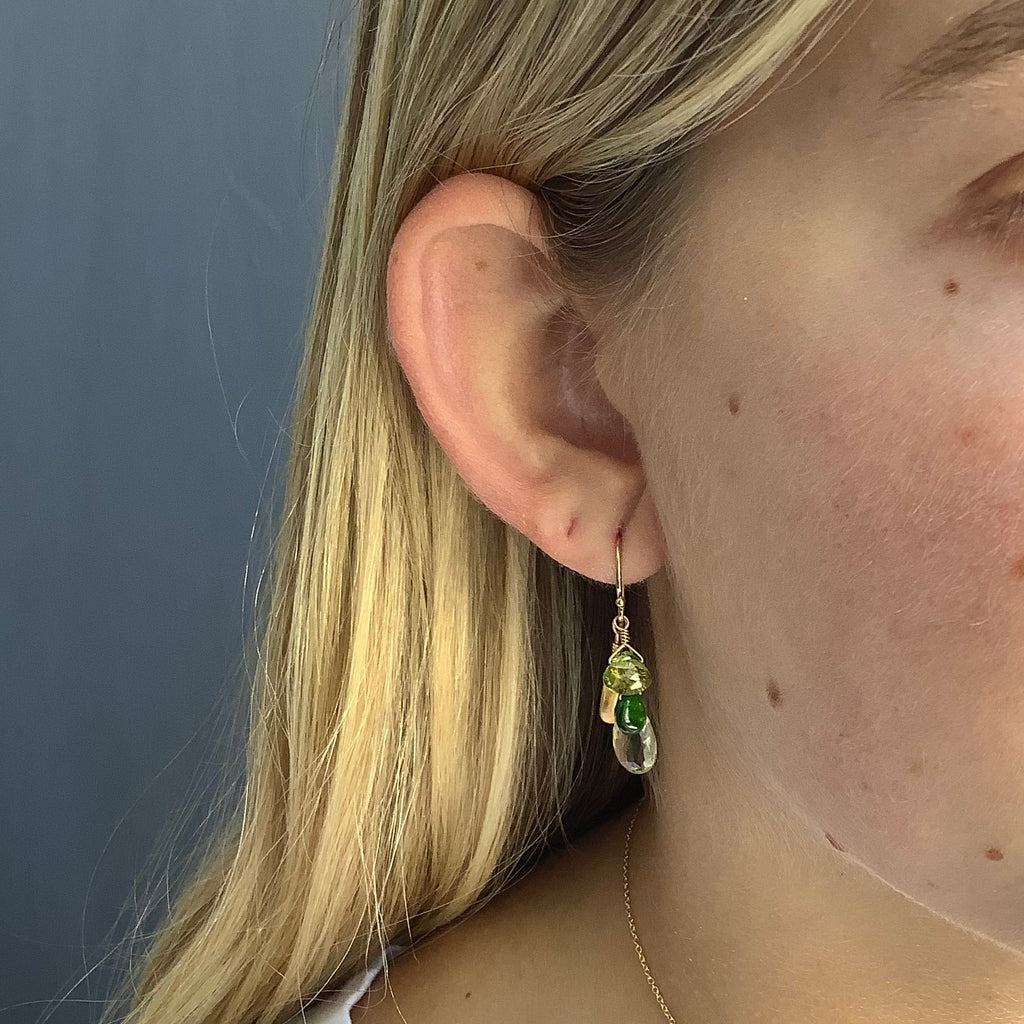 Close-up of a person wearing an earring with a green gemstone on a neutral background