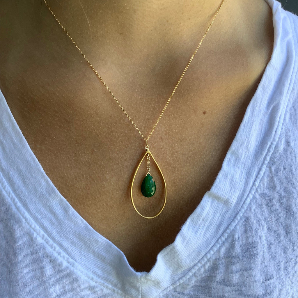 Gold necklace with a green pendant on a person wearing a white shirt.