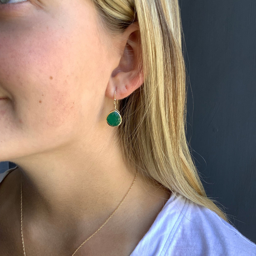 Close-up of a person wearing green earrings with a neutral background