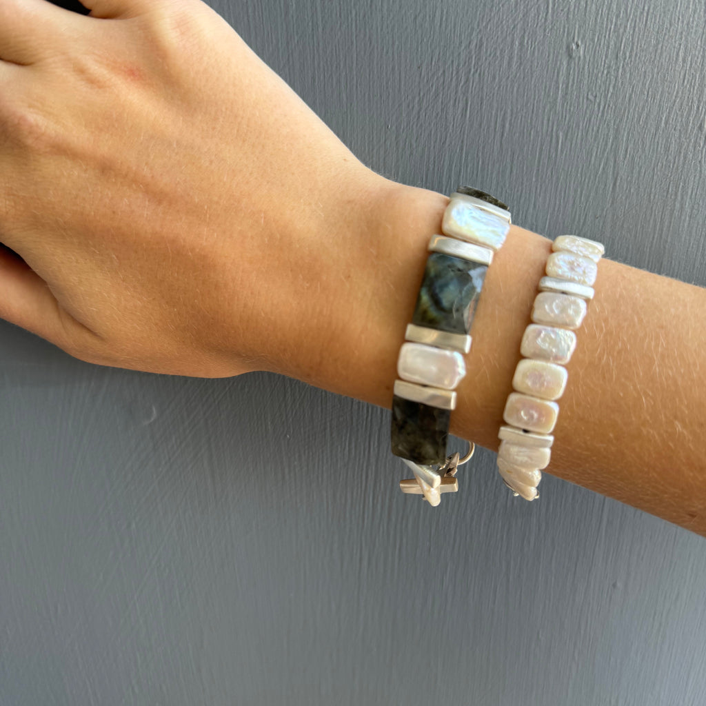 Hand wearing two bracelets on a gray background