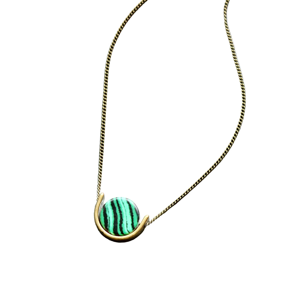 Necklace with a green and gold pendant on a gray surface