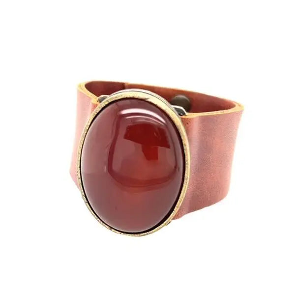 A red leather cuff bracelet with a large oval centerpiece, featuring an antique brass rim.