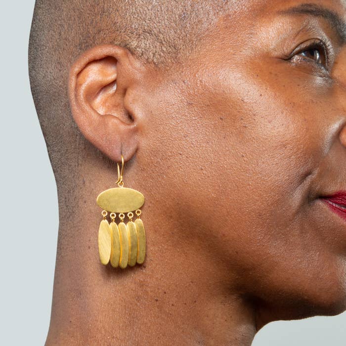 Close-up of a model wearing gold hoop earrings with a light gray background