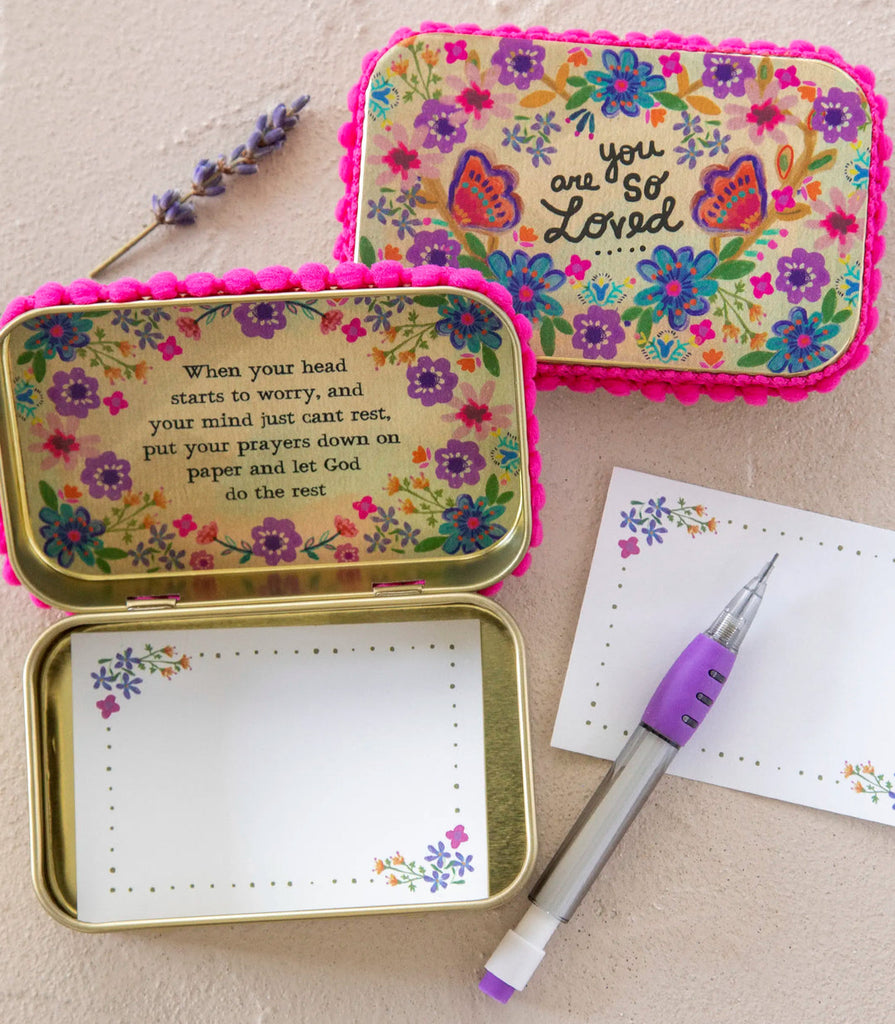 Decorative tin with floral designs and inspirational text, open to reveal a pen and paper inside.