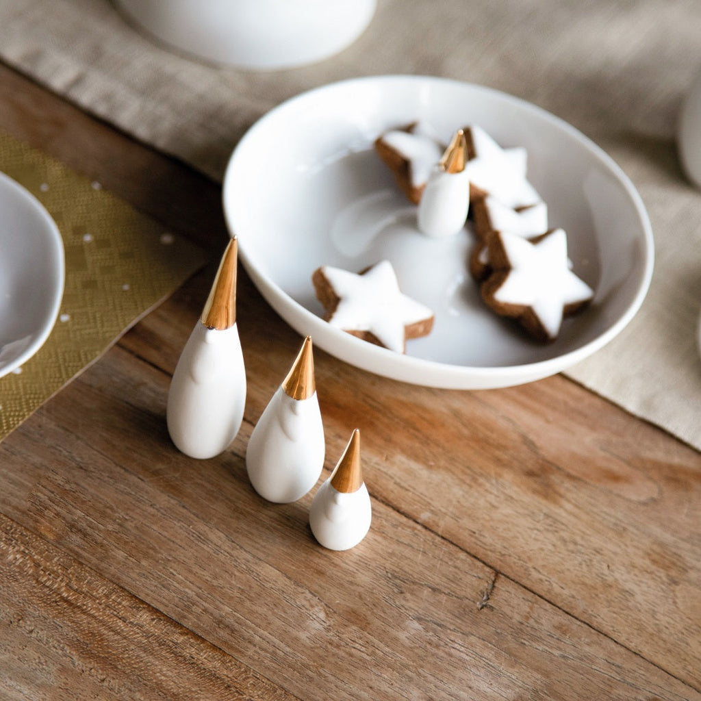 3 white santa gnomes with gold hats on table near white dish with star cookies