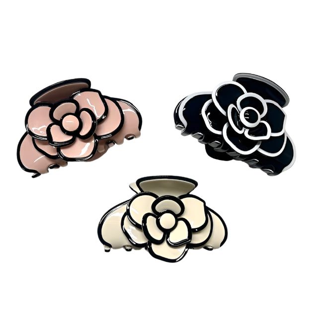 Three floral-shaped hair clips in black, white, and pink on a light gray background