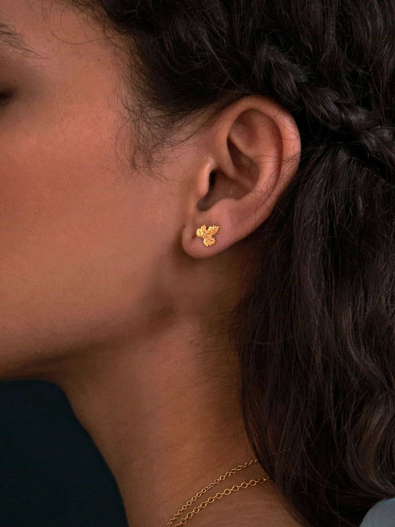 Close-up of an ear wearing a gold earring with dark hair and a blurred background
