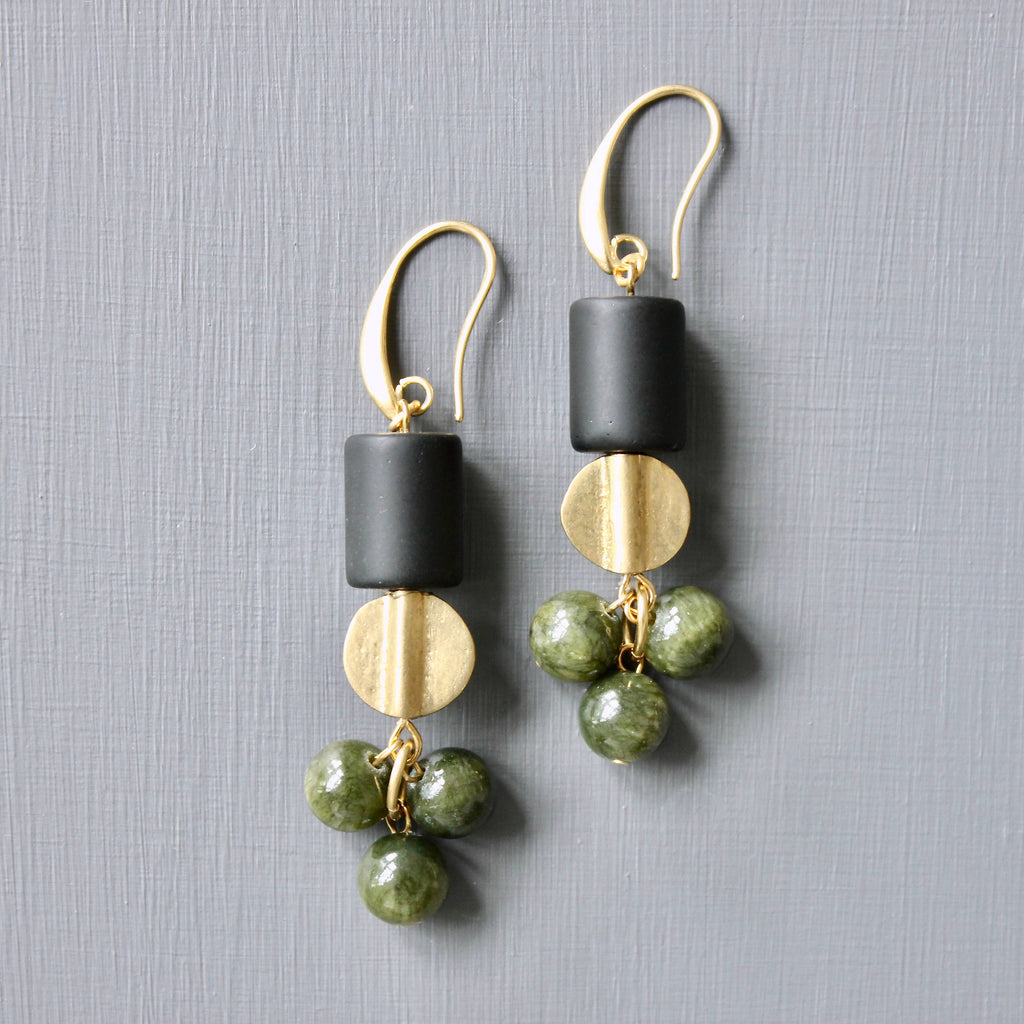 Pair of earrings with black, gold, and green beads on a gray background