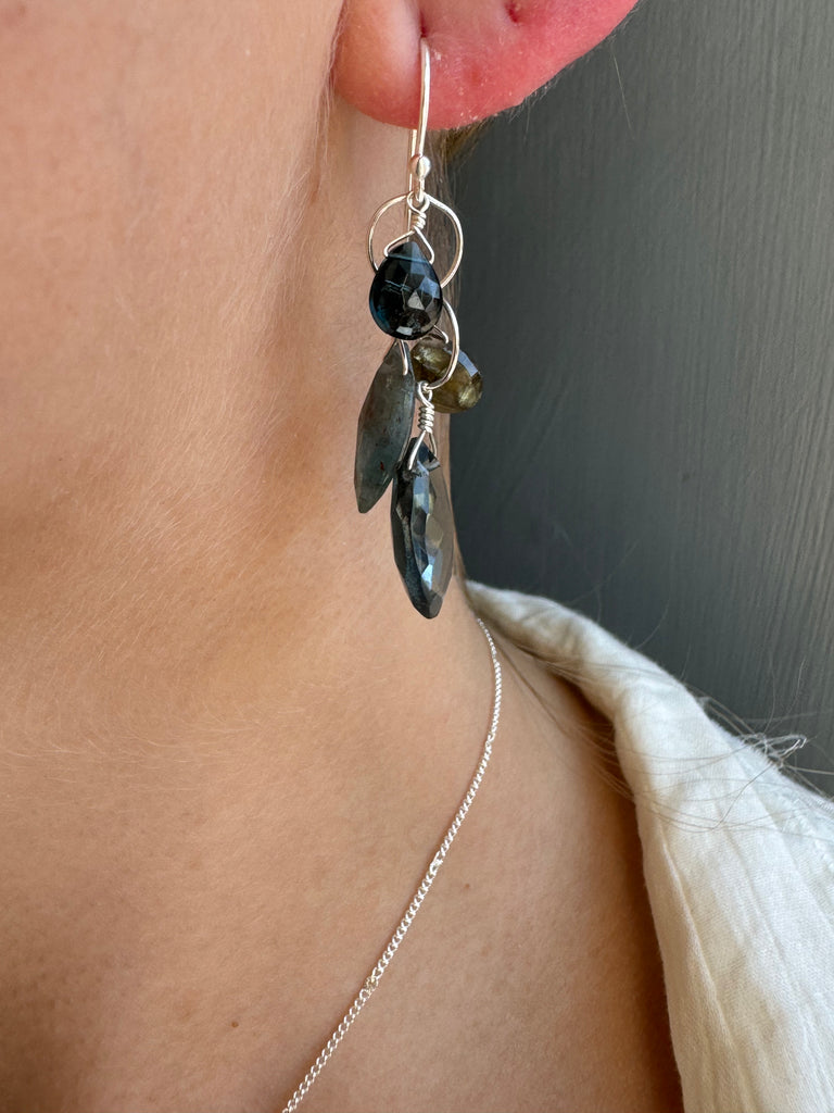 Close-up of a person wearing a silver earring with black and green stones on a plain background.