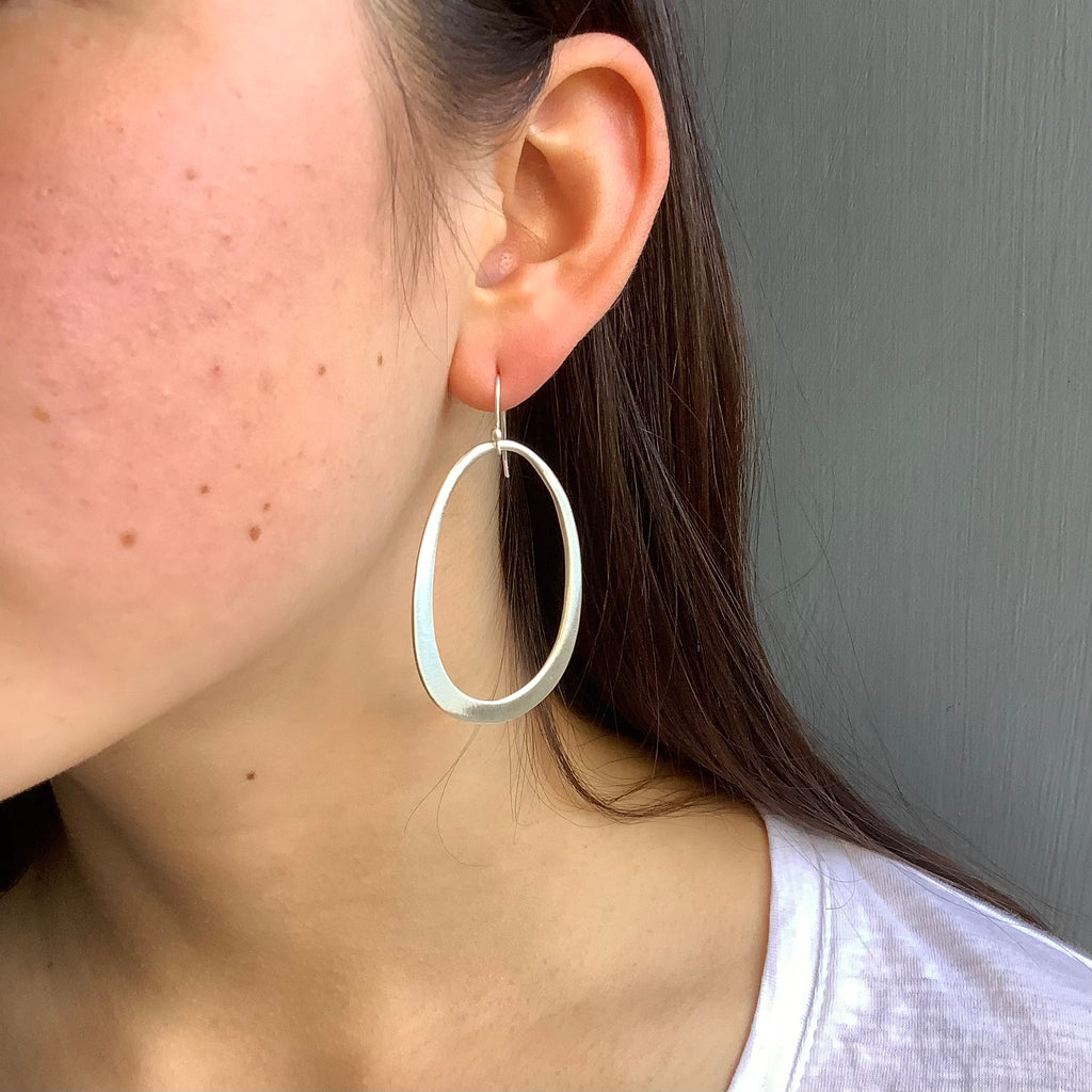 large oval earrings in silver on the ear