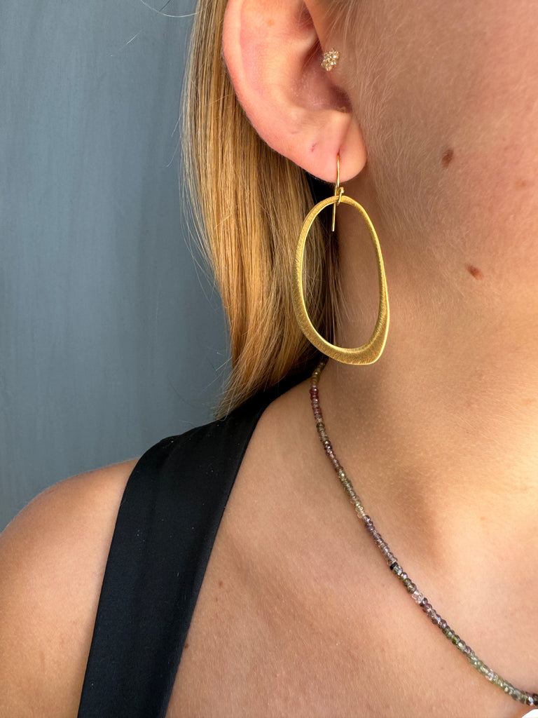 Close-up of a person wearing gold hoop earrings with a neutral background