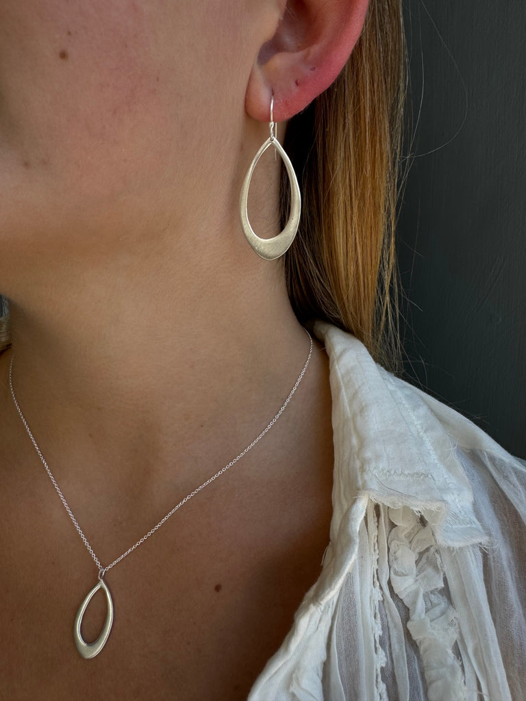 Close-up of a person wearing a delicate silver chain with an oval pendant and oval earring