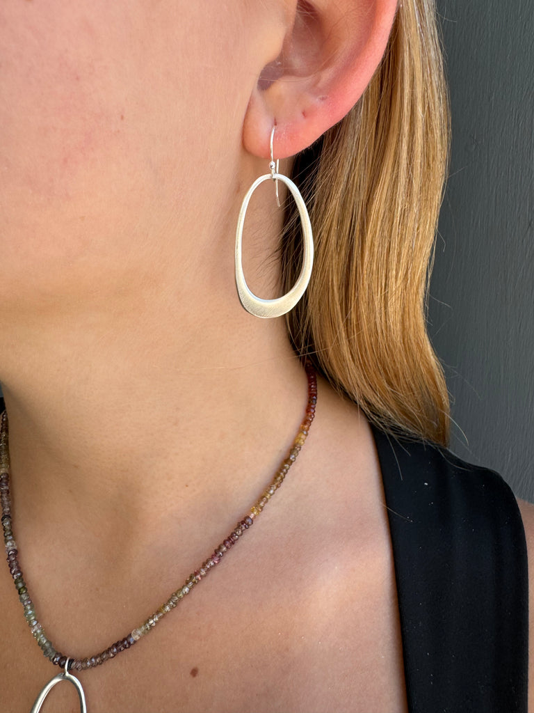 Close-up of a person wearing a large hoop earring and a beaded necklace against a dark background.