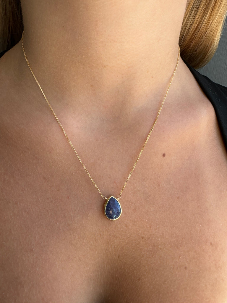 Gold necklace with a blue pendant on a person's neck