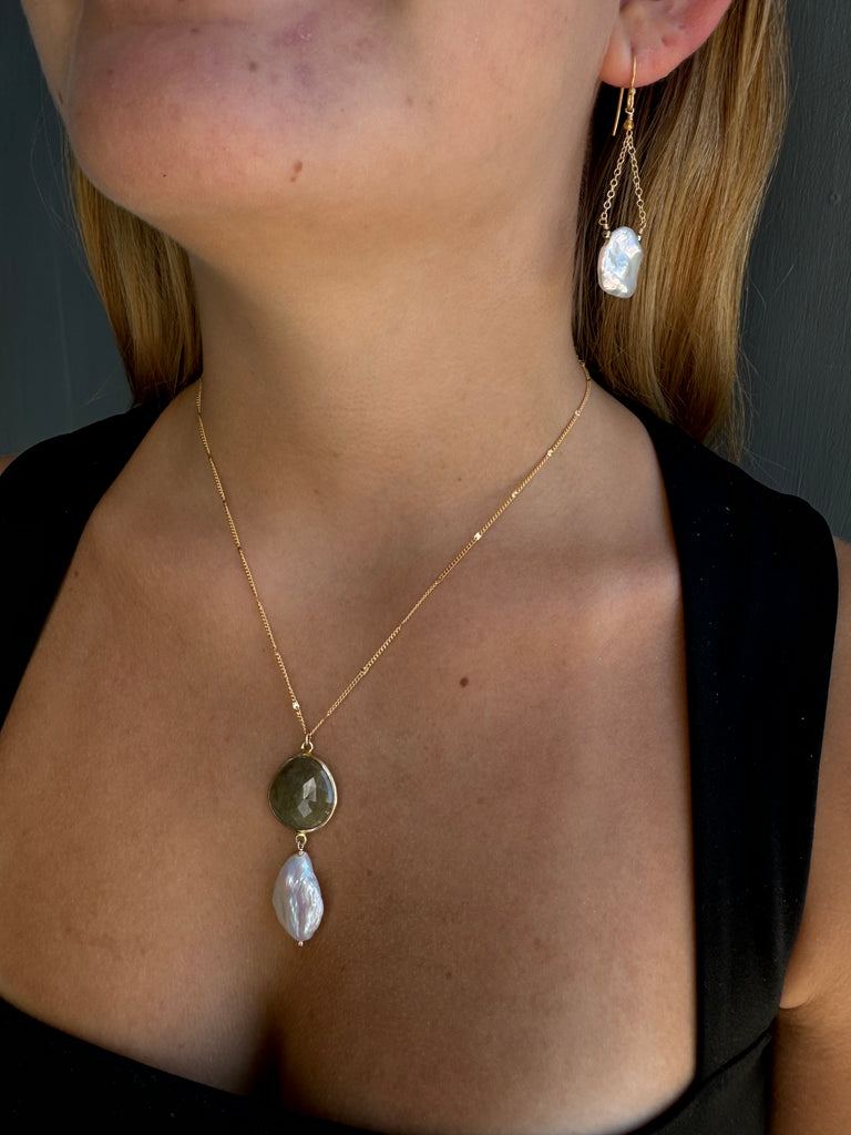 Close-up of a gold necklace with yellow sapphire station and white pearl on a person's neck.