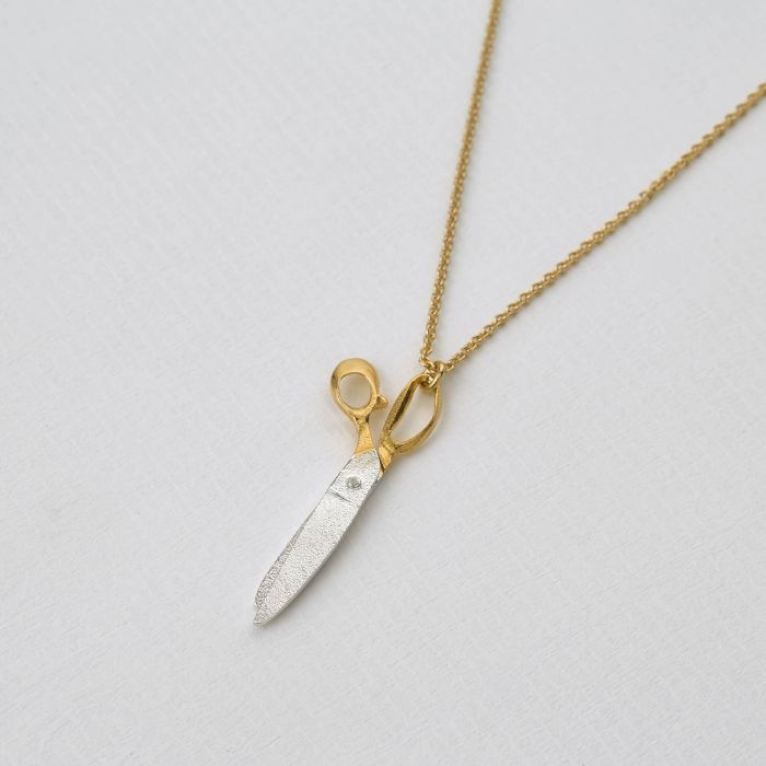 shearing scissors necklace resting on textured white background