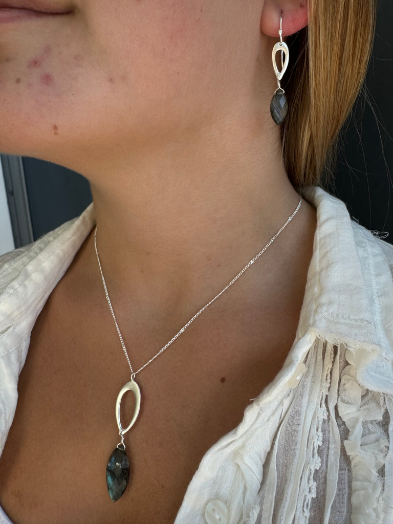 Necklace with pendant on a person wearing a white lace garment with matching earring