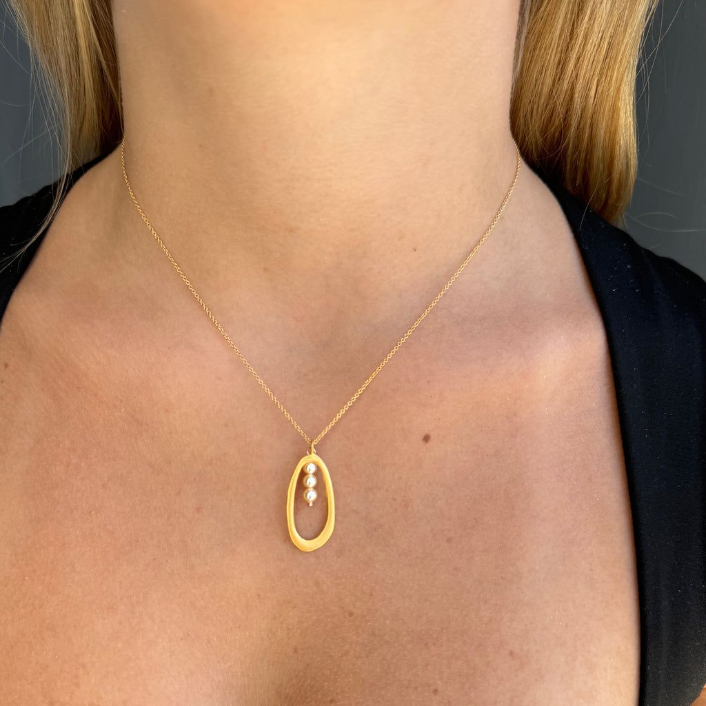 Gold necklace with a pendant worn by a person against a neutral background