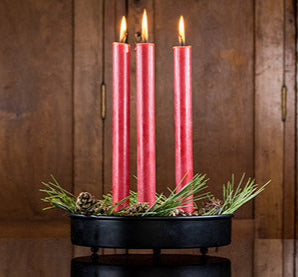 Three lit red candles in tray with greenery