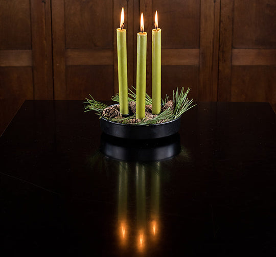 Three lit green candles in a decorative holder on a dark surface with a wooden background