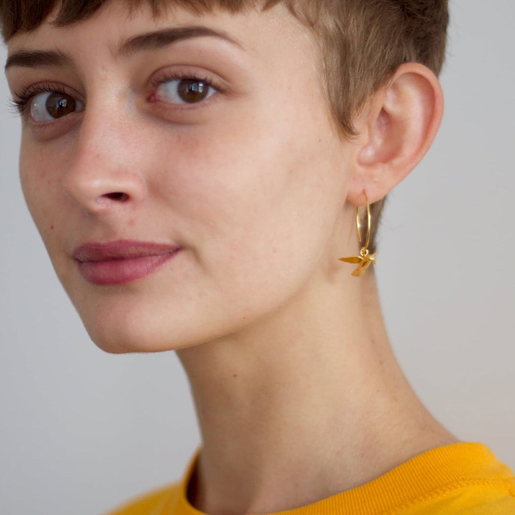 Close-up of a person wearing gold earrings with a neutral background