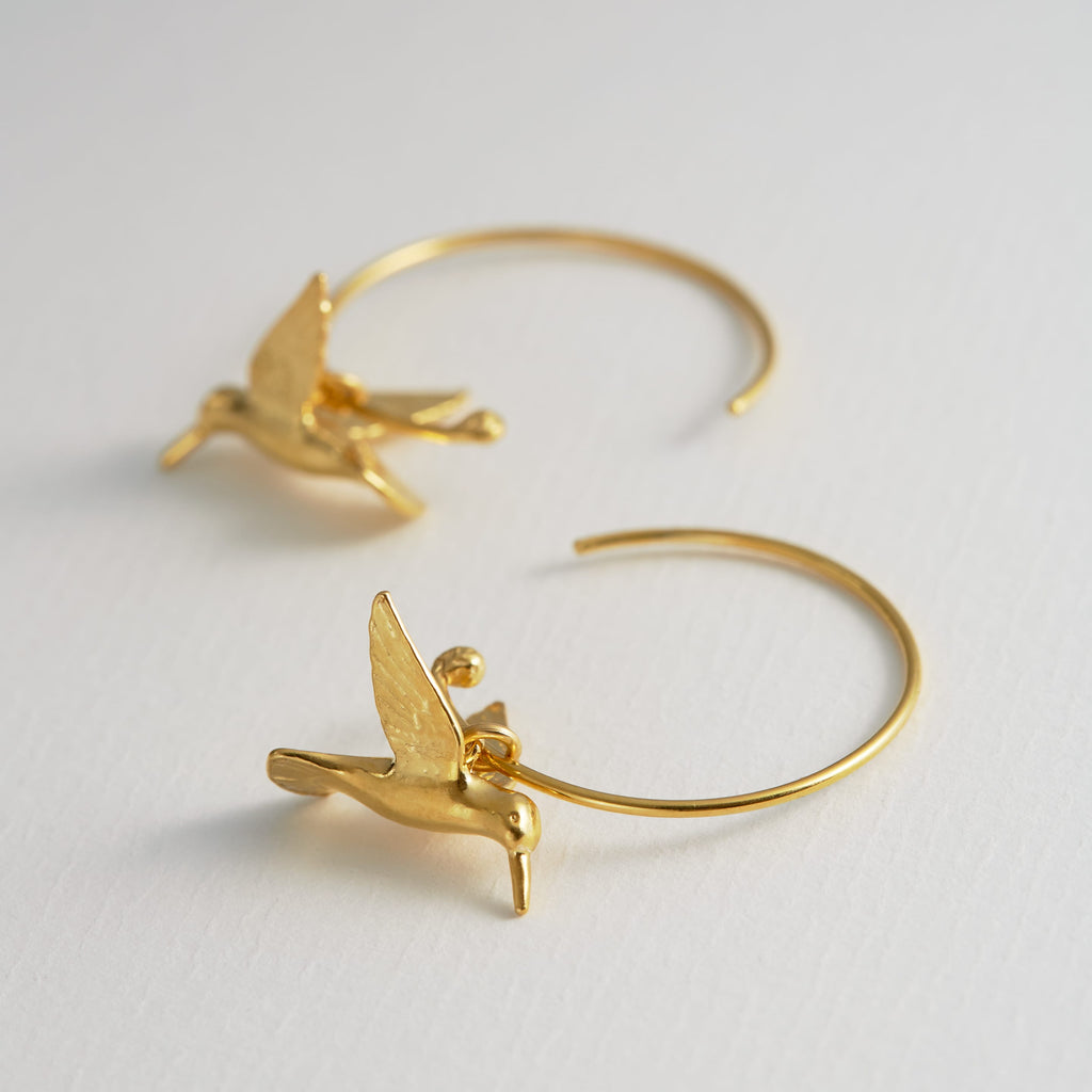 Gold hoop earrings with bird designs on a light gray background
