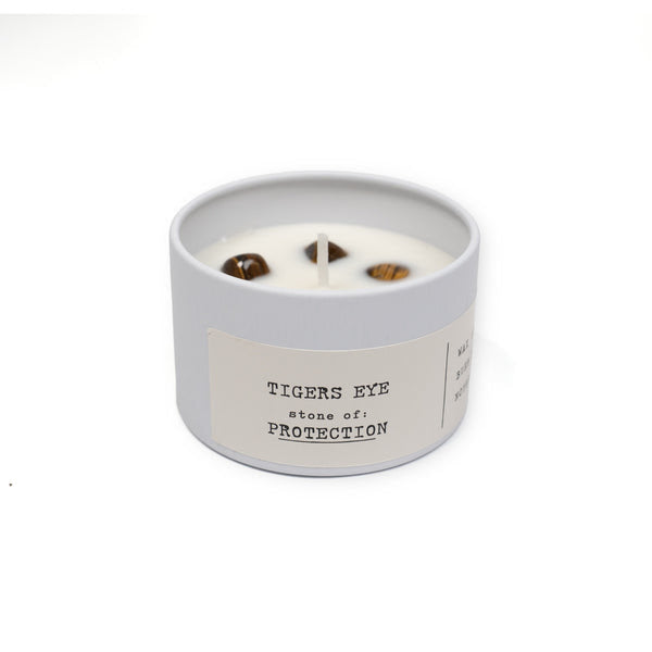 white candle in tin with tigers eye on white background