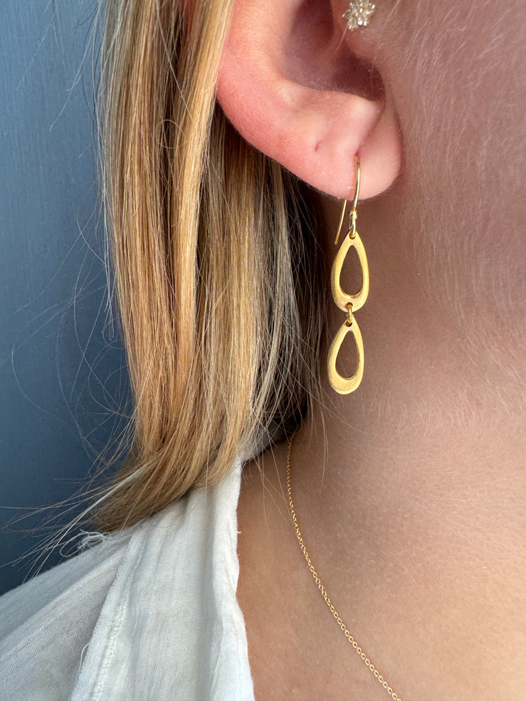 Gold double drop earring being worn on a person's ear with a neutral background