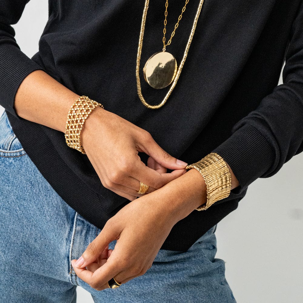 Person wearing gold jewelry including a necklace, bracelet, and ring on a neutral background