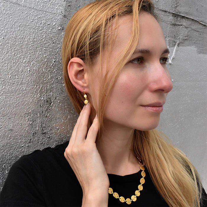 Tiny Double Disc Drop Earrings in Gold plating on model on gray stone background